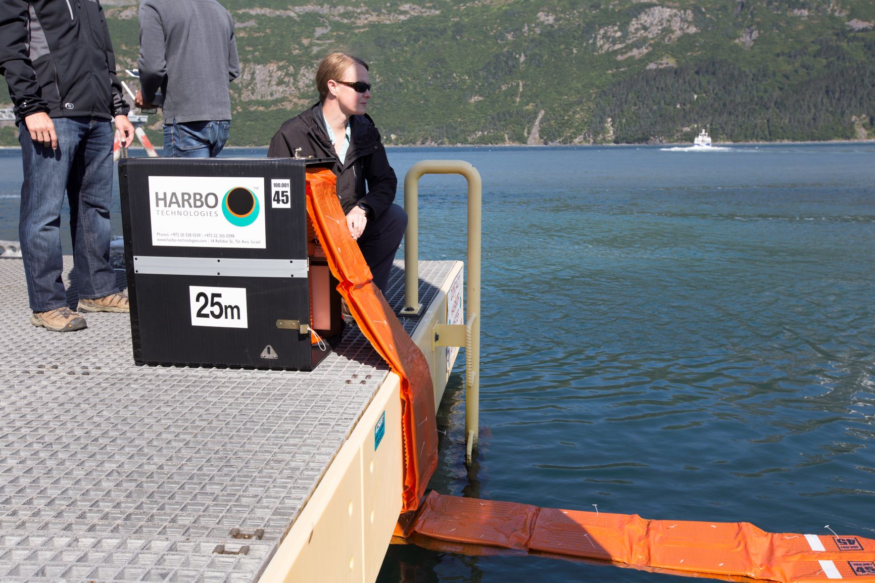 a person deloploying a HARBO boom out of a cartridge on a quay in a fjord